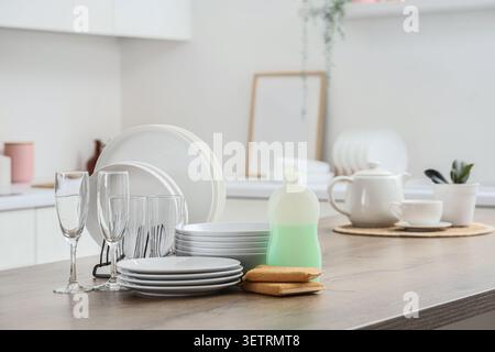 Clean white dishes and glasses drying on kitchen counter with dish soap and sponges Stock Photo