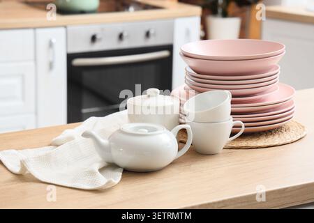 Stack of pink plates and white teapot with cups on kitchen counter Stock Photo