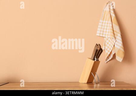 Wooden knife block with knives and hanging kitchen towel on beige wall Stock Photo
