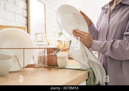 Person drying a white plate with a towel in kitchen Stock Photo