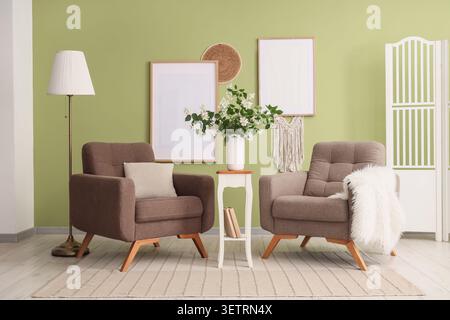 Cozy living room with two brown armchairs and decorative elements on green wall Stock Photo