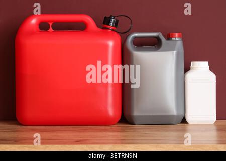 Three plastic jerry cans of different sizes and colors on wooden surface Stock Photo