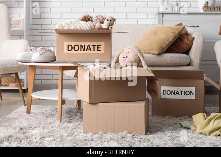Cardboard boxes filled with clothes and toys for donation in cozy living room Stock Photo