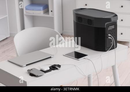 Portable power station charging multiple electronic devices on white desk Stock Photo
