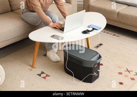 Person working on laptop with multiple devices charging on portable power station at home Stock Photo