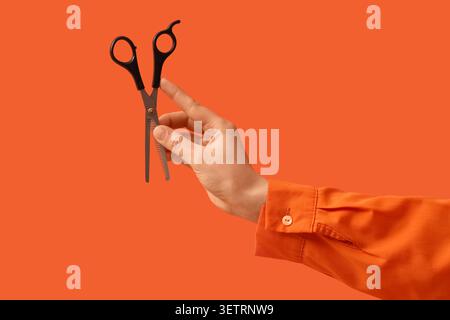 Hand holding thinning scissors on orange background Stock Photo