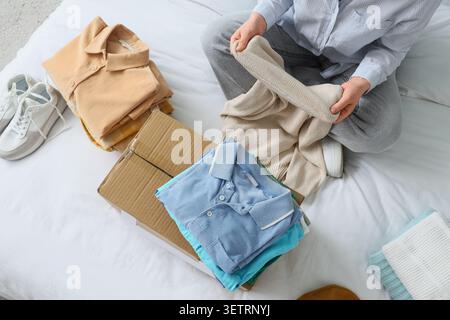 Person folding clothes on bed with cardboard box Stock Photo