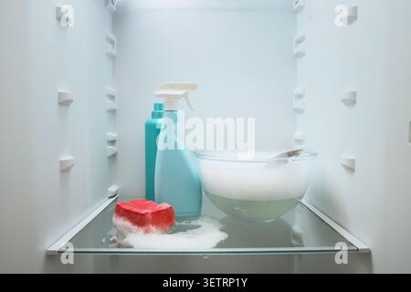Cleaning supplies and soapy water inside an empty refrigerator Stock Photo