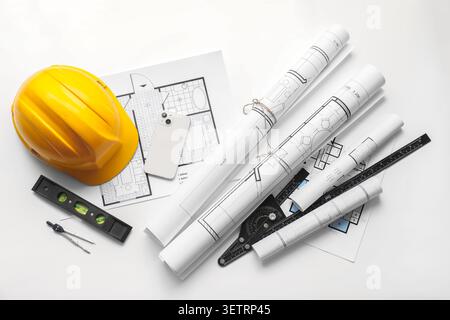 Architectural blueprints with yellow construction helmet and drafting tools on white background Stock Photo