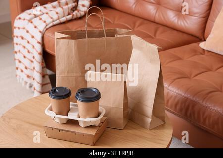 Eco-friendly takeout coffee cups and paper bags on wooden table in cozy living room Stock Photo