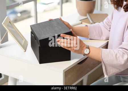 Woman opening black gift box at desk Stock Photo