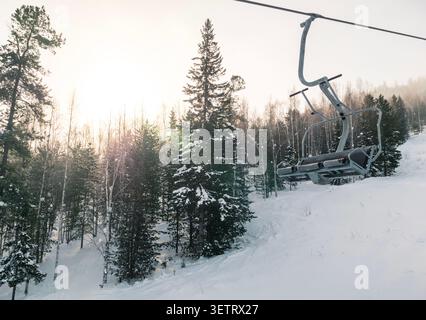 Ski lift descends through snow-covered trees in mountain landscape during sunrise Stock Photo
