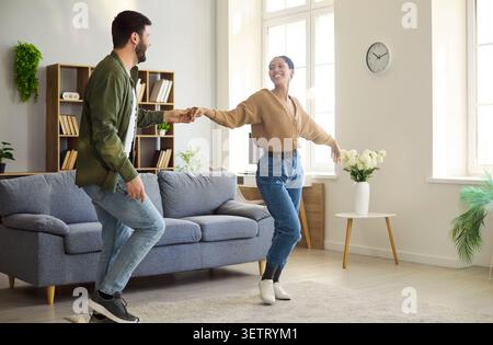 Happy couple dancing at home in bright living room, playful mood and love Stock Photo