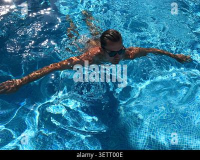 High-angle close-up of an attractive young man swimming in beautiful, clear blue water. A vibrant and refreshing summer holiday concept. Stock Photo
