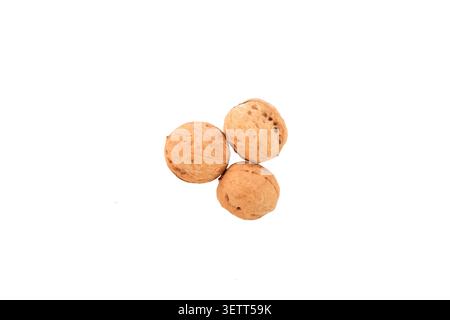 Three whole walnuts with textured, warm brown shells are clustered together against a plain, neutral light gray background, highlighting their natural Stock Photo