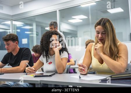 Focused young students actively participating in a group learning session at desks in a contemporary classroom, engaged in study activities with a tea Stock Photo