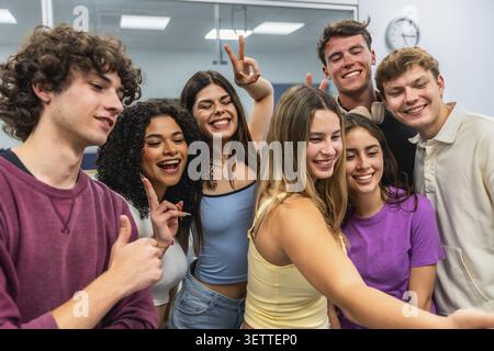 Happy, diverse group of young students smiling and posing for a selfie in a bright classroom, showcasing friendship, unity, and positive collaboration Stock Photo