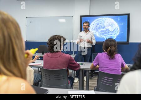 Professor lecturing a diverse group of students in a modern classroom, using an interactive digital screen displaying a 3d human brain model for neuro Stock Photo