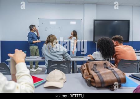 Professor explaining mathematical concepts on a whiteboard to a diverse group of college students attentively listening and taking notes during a high Stock Photo