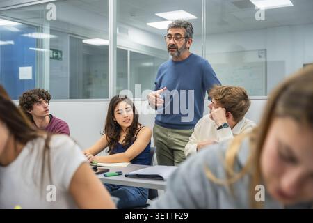 Experienced teacher actively engaging with a group of diverse university students, fostering an interactive learning and discussion environment in a b Stock Photo