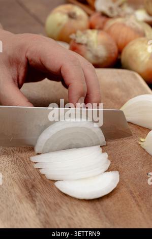Close up of hand slicing fresh onion on a wooden cutting board Stock Photo