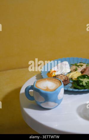 Blue cloud patterned mug with latte art beside colorful brunch plate on white table Stock Photo