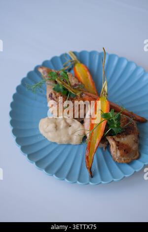 Gourmet roasted chicken with glazed carrots, herbs and creamy sauce on blue plate Stock Photo