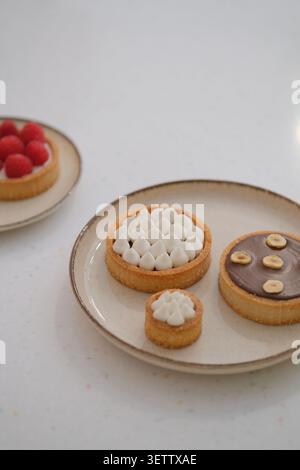 Elegant assortment of small pastry tarts on ceramic plates with cream, chocolate, and raspberries Stock Photo