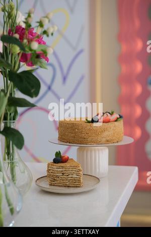 Elegant layered dessert cake on white stand with fresh berries beside soft floral decor Stock Photo