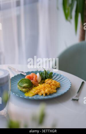 Elegant breakfast plate with scrambled eggs, avocado, smoked salmon, herbs on bright table Stock Photo
