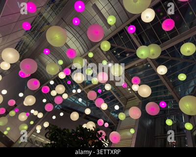 Glowing pink, green, and white paper lanterns hang beneath a glass atrium, creating a vibrant night interior with an upward view. Stock Photo