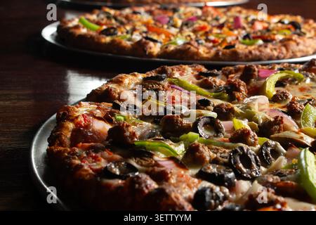 A closeup view of some pizzas on a restaurant table, featuring a deluxe pizza. Stock Photo