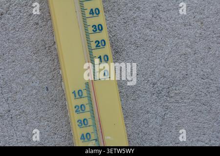 A bright yellow thermometer displays temperature readings on a gray textured surface indicating warm weather conditions in an outdoor setting on a sun Stock Photo