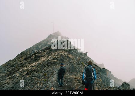 A Group of Hikers Standing on the Volcanic Rim above the clouds on a foggy day in the Alpine Desert Zone of Mount Meru, Arusha National Park, Tanzania Stock Photo