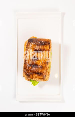 A mouth-watering grilled panini sandwich with a golden crispy crust and fresh vegetable filling, presented on a sleek rectangular ceramic platter Stock Photo