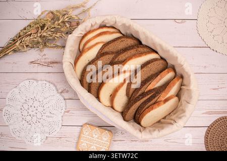 A high-angle view of a rustic basket filled with various slices of fresh white and rye bread. The basket is set on a light wooden background, decorate Stock Photo