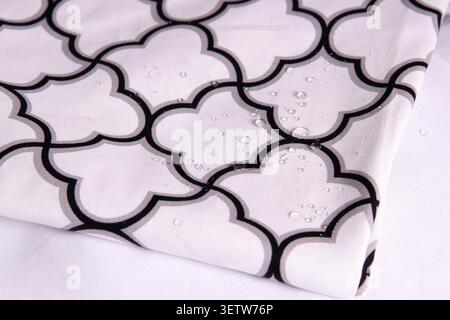 A close-up view of a high-quality white textile with a geometric Moroccan trellis pattern, featuring clear water droplets on the surface to demonstrat Stock Photo