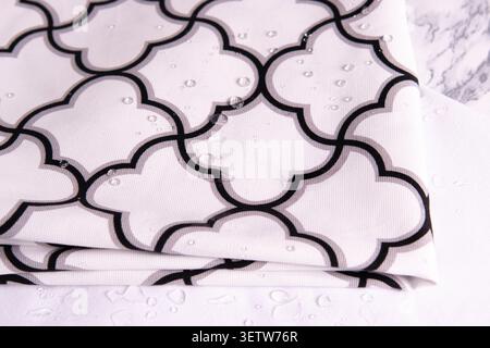 A close-up view of a high-quality white textile with a geometric Moroccan trellis pattern, featuring clear water droplets on the surface to demonstrat Stock Photo