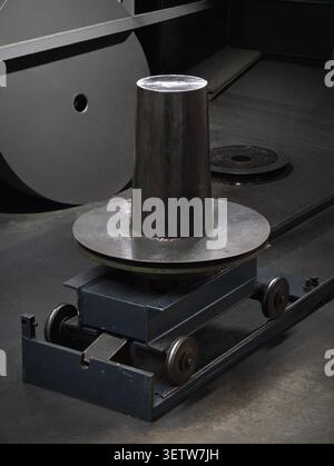 Close view of industrial metal bollard mounted on circular and wheeled rail platform inside workshop. Heavy cylindrical steel post with visible weld s Stock Photo