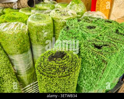 A variety of green artificial turf and moss rolls are neatly stacked and ready for sale, showcasing different textures and shades Stock Photo