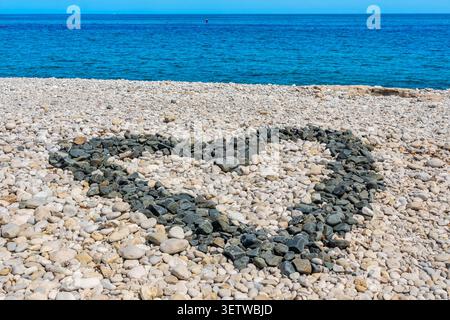 Black heart-shaped pebbles on shore alongside white pebbles Stock Photo