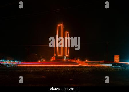 Palu, Indonesia - June 12, 2026 : Nighttime cityscape with glowing vertical structures. Long exposure captures motion blur from passing vehicles. Dark sky contrasts bright architectural lights Stock Photo