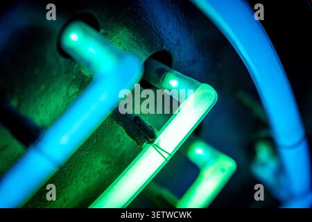 Glowing neon tubing with bent connectors in moody blue green light on dark metal backing Stock Photo