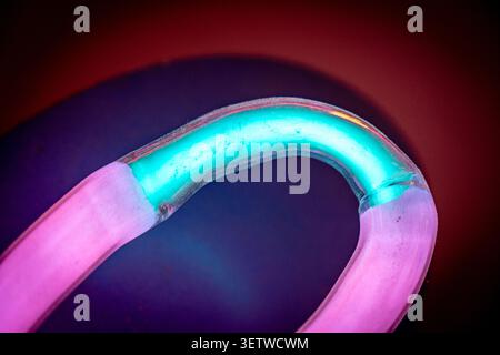 Curved neon glass tube glowing cyan and magenta against dark gradient background with vignette Stock Photo