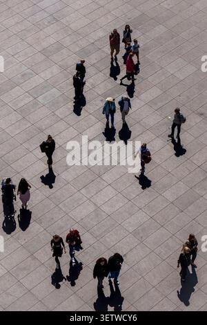High-angle view of pedestrians casting long shadows on sunlit urban plaza in Warsaw Stock Photo