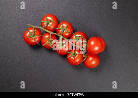 Ripe cherry tomatoes on a vine, showcasing their vibrant red color and natural freshness against a dark textured surface, symbolizing healthy eating a Stock Photo