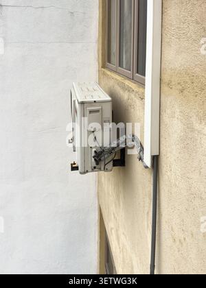 white air conditioner compressor unit mounted on exterior building wall, metal casing with insulated refrigerant pipes, side view with copy space Stock Photo