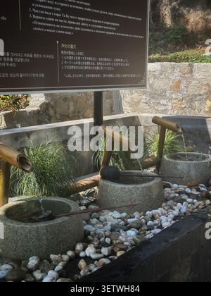 Traditional bamboo water fountain with stone basins for ritual purification. A serene asian temple fountain featuring bamboo pipes flowing into stone Stock Photo