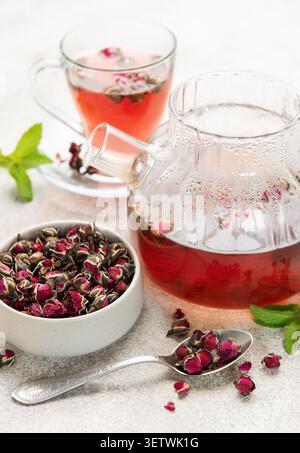 Rose tea brewing in a glass teapot and cup with dried buds and fresh mint Stock Photo