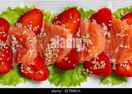 Gourmet salmon tataki salad with red strawberry slices and sesame seeds on lettuce. Beautiful texture backdrop for restaurant menu catering promotion Stock Photo